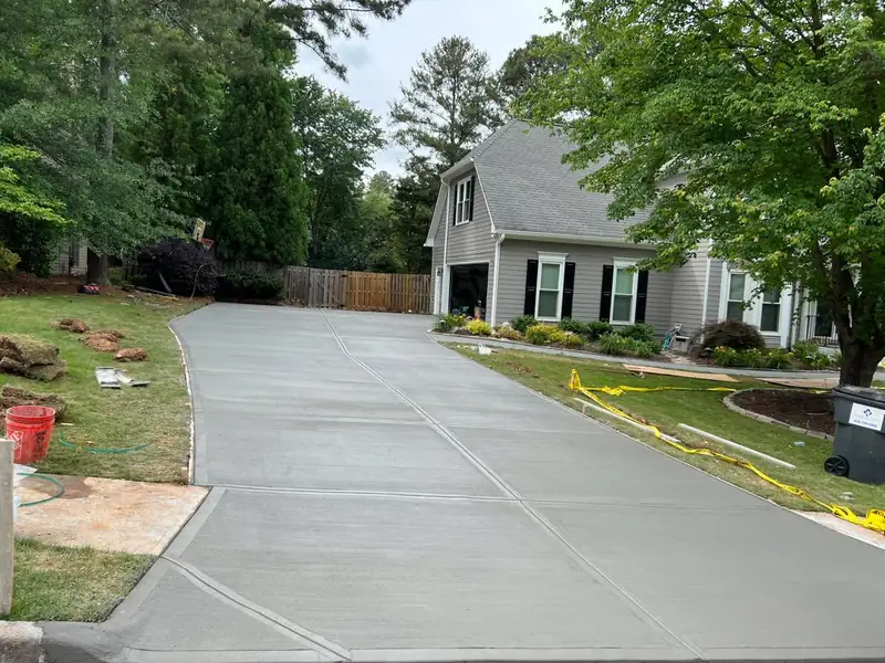 Long broom-finish concrete driveway with diagonal control joints leading up to a gray house