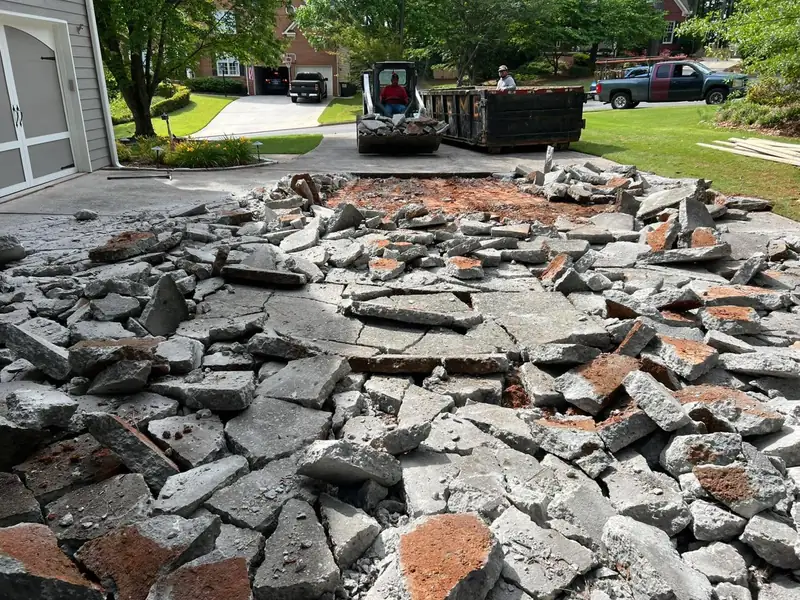 Broken-out old driveway rubble with an excavator and dumpster at the street