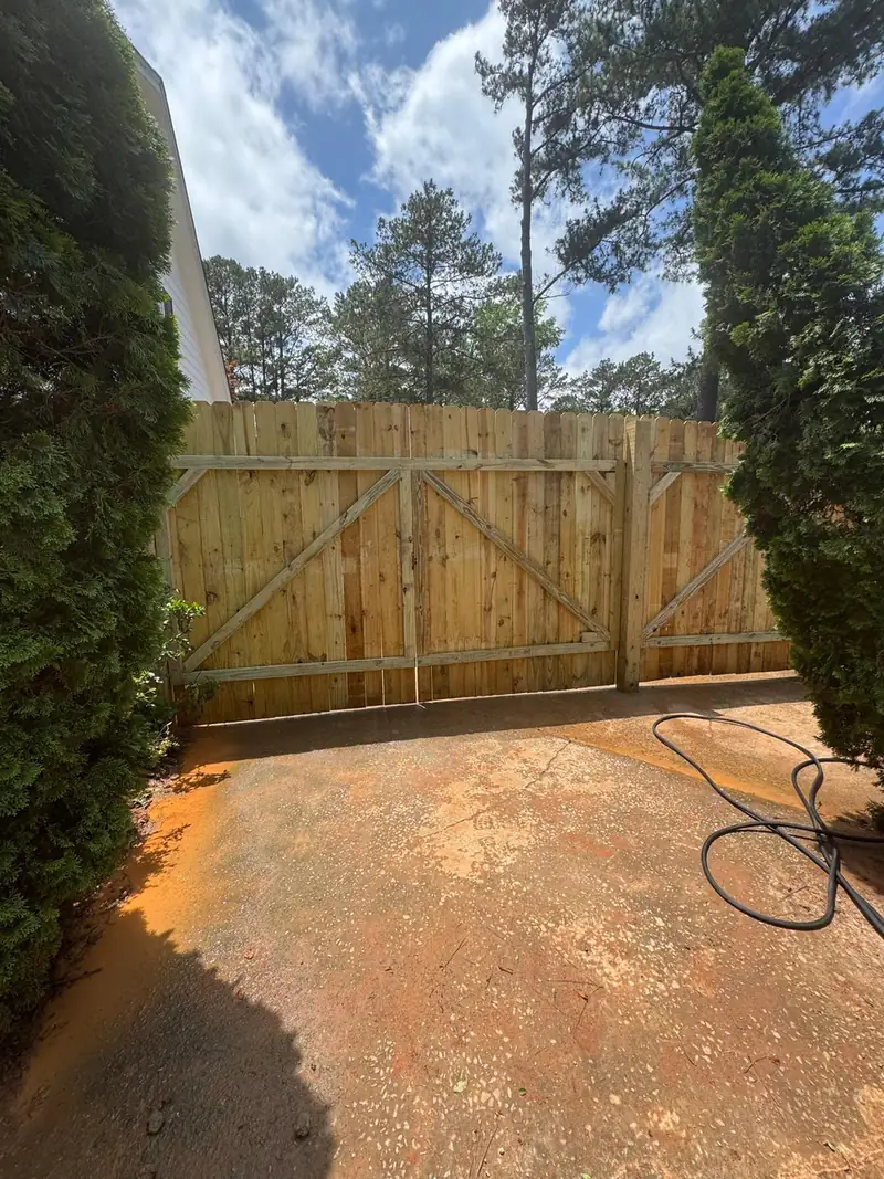 New wood privacy fence with a double gate at the end of a dirt drive
