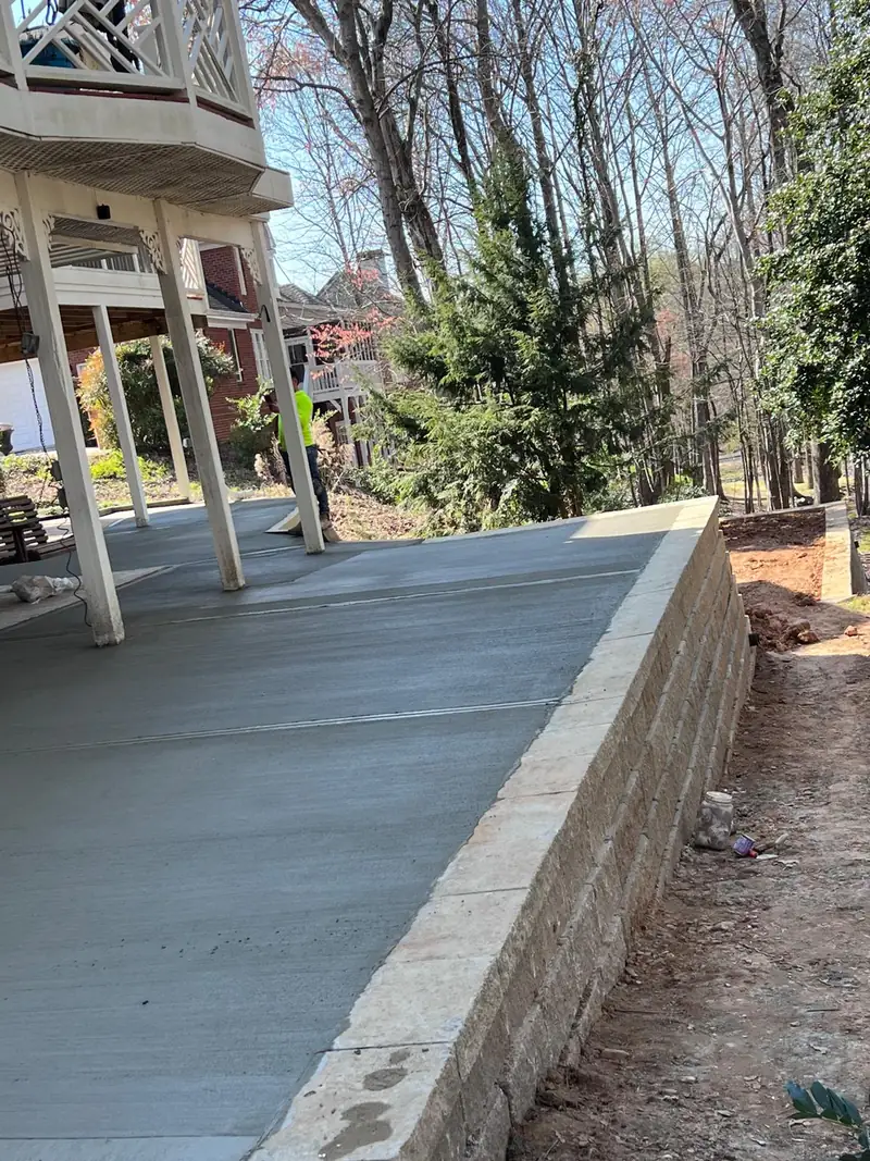 Concrete slab under a deck beside a block retaining wall on a wooded lot