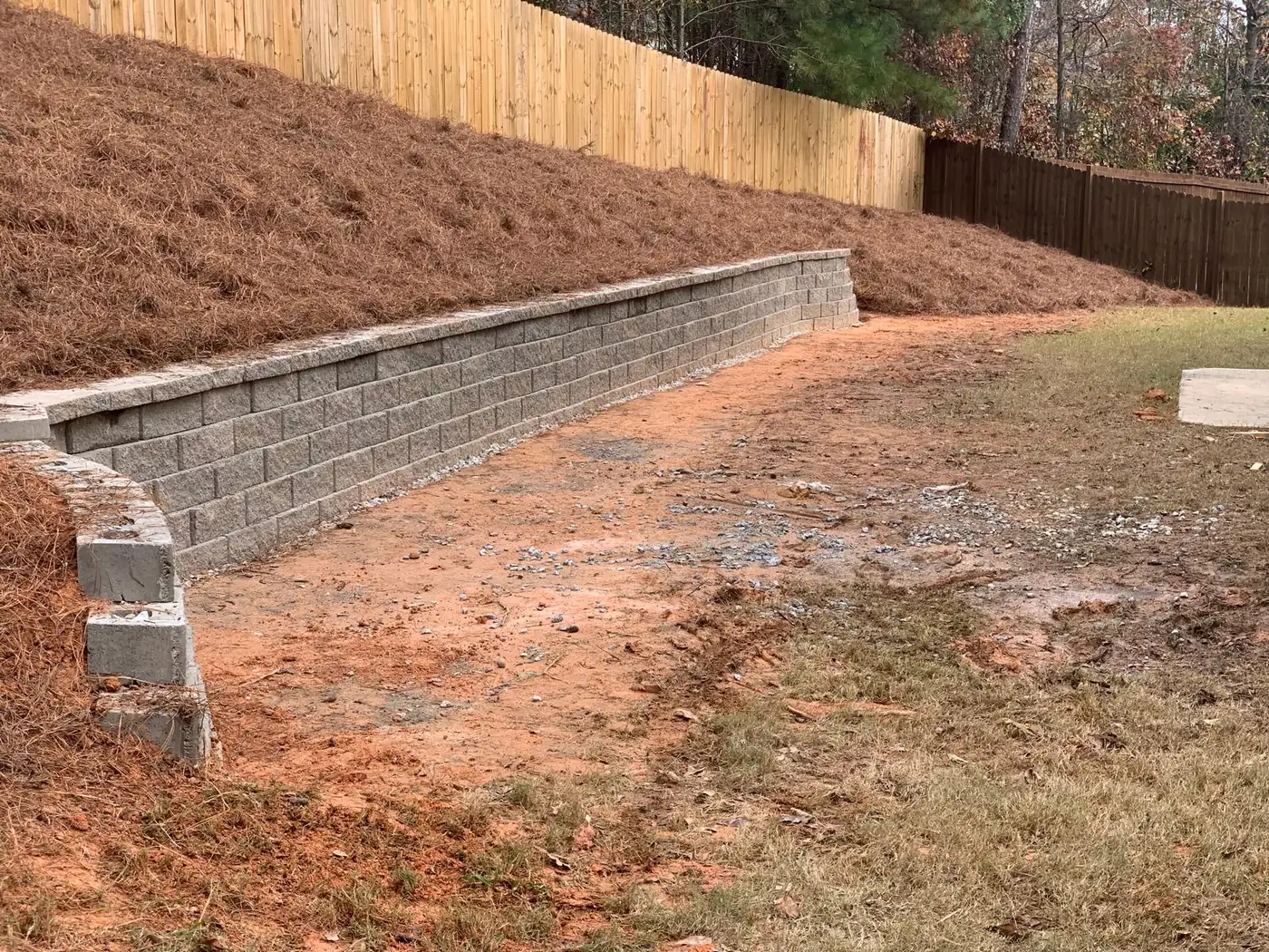 Block retaining wall along a graded slope with a fence above