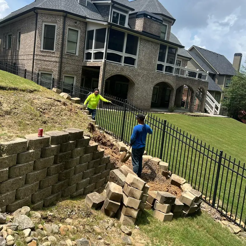 Crew building a segmental block retaining wall below a stone house