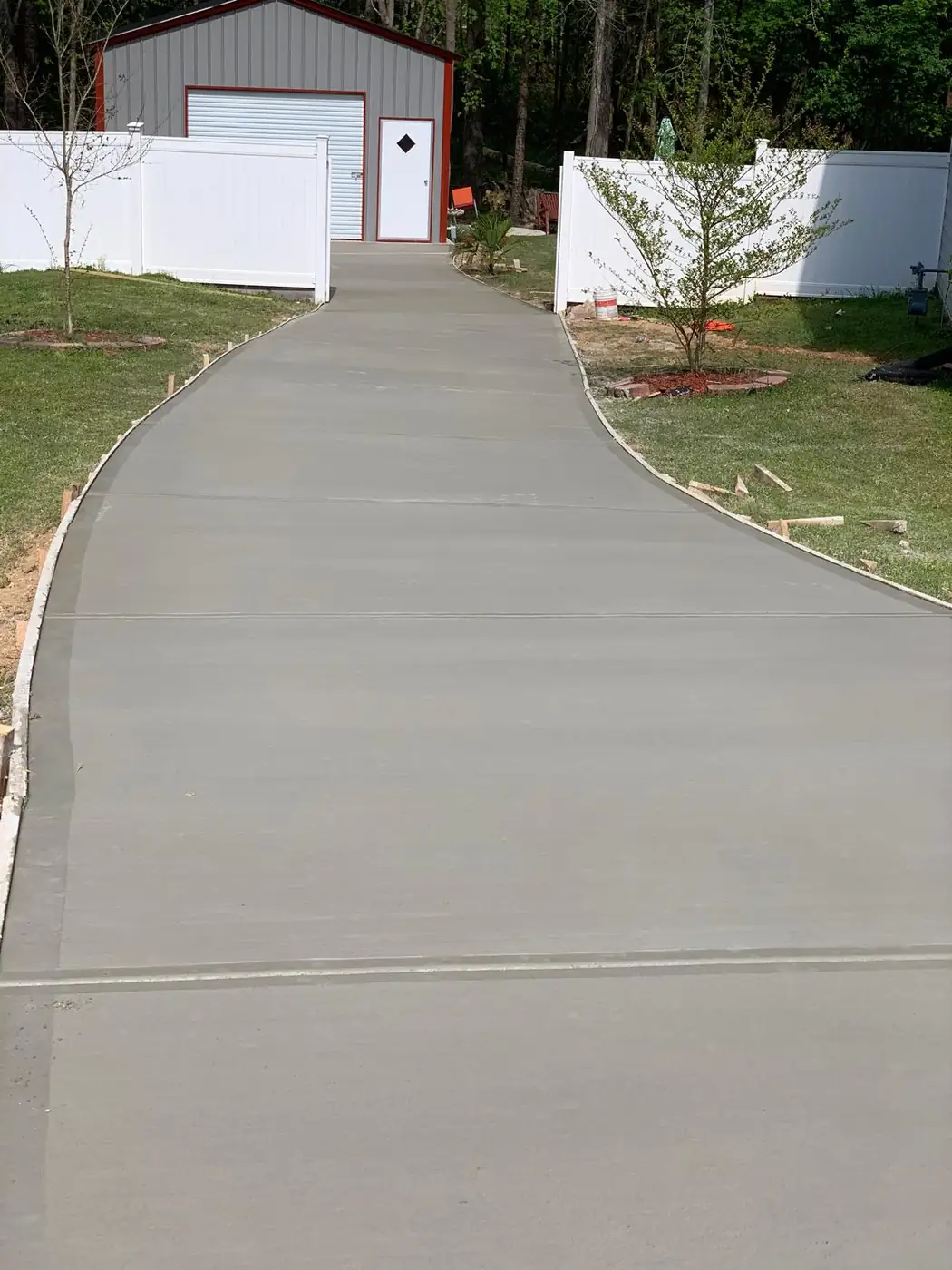 Long curving concrete walkway to a white garage beside a vinyl fence