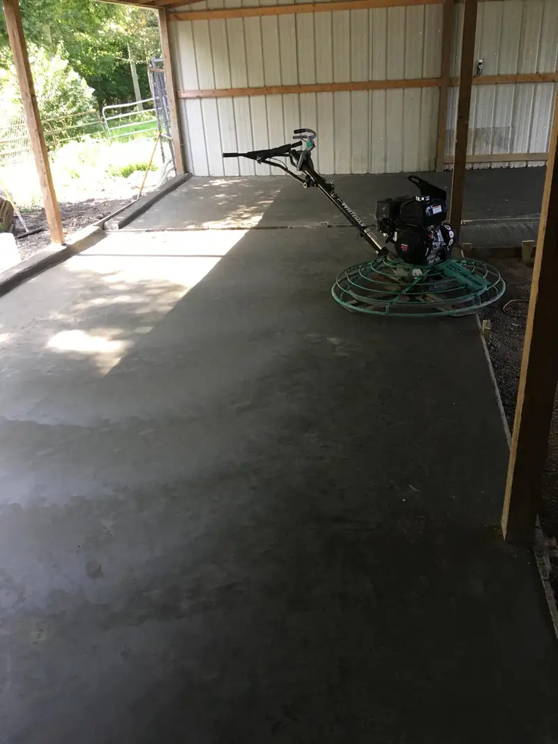 Power trowel finishing a concrete floor slab inside a pole barn