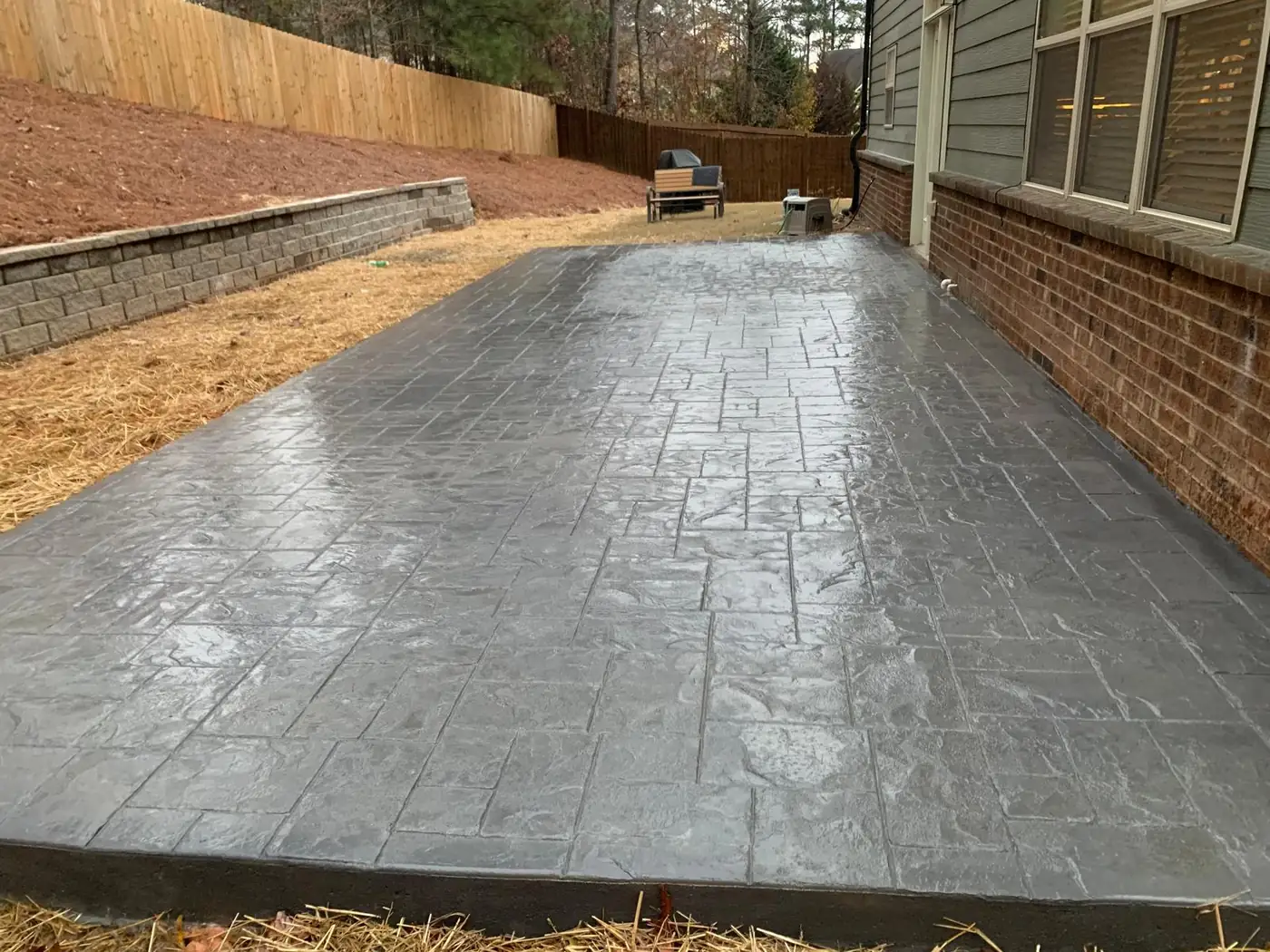 Gray stamped concrete patio in an ashlar stone pattern along a brick house