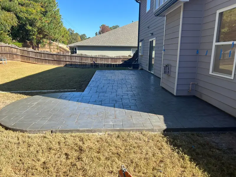 Curved gray stamped concrete patio behind a house in a fenced yard