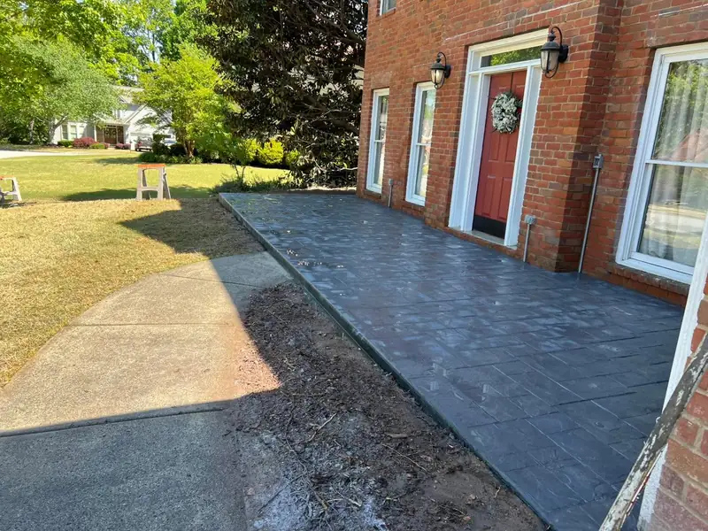Gray stamped slate-pattern concrete walkway along a red-brick house with a red door